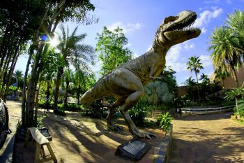 A dinosaur stands in a sunny park.