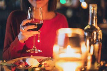 Someone wearing red holds a glass of red wine, sitting at a dinner table.