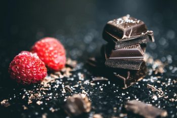 Pieces of chocolate sit next to a raspberry.